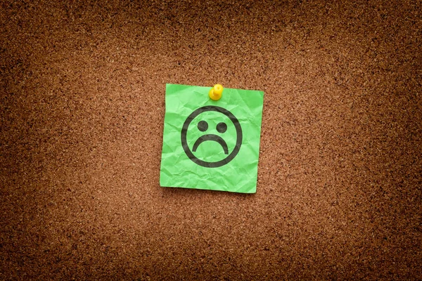 Green paper note with sad face on a cork board — Stock Photo, Image