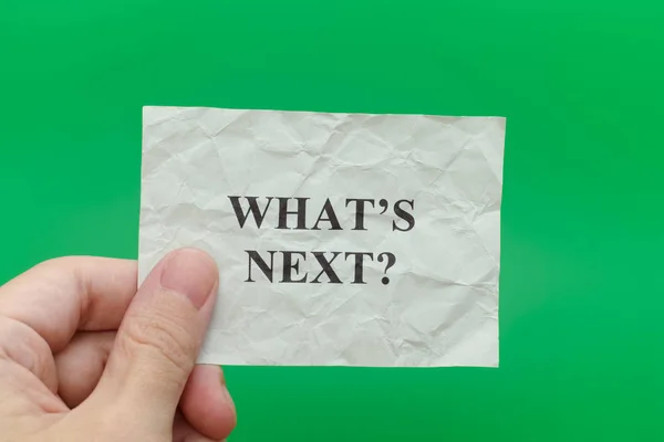 Person holding grey paper note with question What is next — Stock Photo, Image