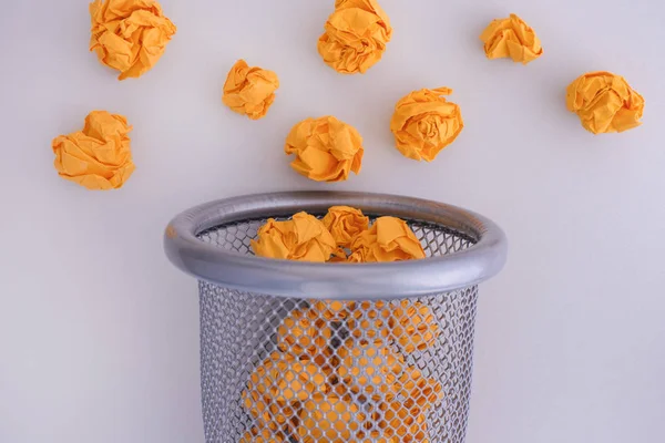 Bolas de papel amarelas enrugadas rolando para fora de uma lata de lixo — Fotografia de Stock