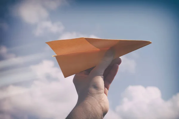 Aereo di carta in una mano contro cielo nuvoloso — Foto Stock