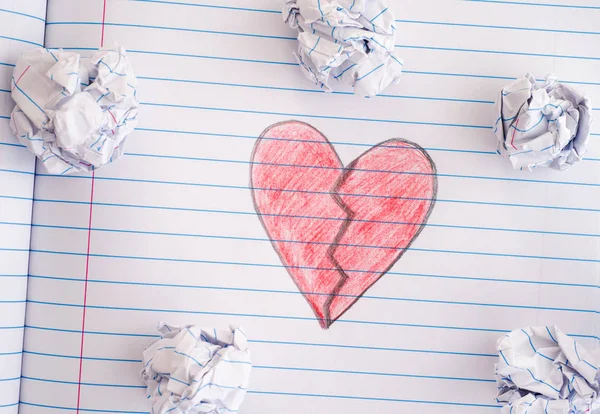 Corazón roto en la hoja del cuaderno con algunas bolas de papel arrugado en — Foto de Stock