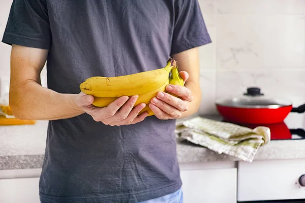Uomo in piedi in cucina e tenendo le banane nelle sue mani — Foto Stock