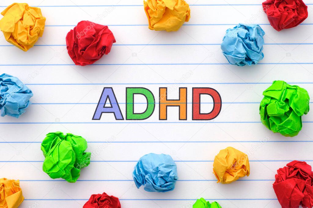 ADHD. Abbreviation ADHD on notebook sheet with some colorful crumpled paper balls around it. Close up. ADHD is Attention deficit hyperactivity disorder.