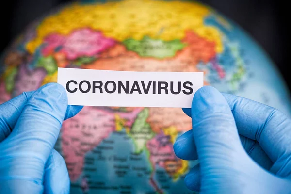 Orvosi Kesztyűben Tartja Coronavirus Szót Kezében Egy Földgömbbel Szemben Közelről — Stock Fotó