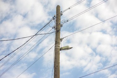 Elektrik direğinde lamba ve elektrik kabloları asılı. Bulutlu gökyüzü.