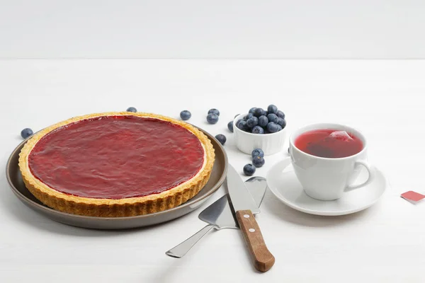 Homemade cheesecake with berry jelly and cup of red tea hibiscus on white wooden table.