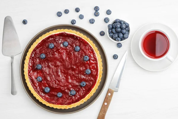 Homemade cheesecake with berry jelly and cup of red tea hibiscus on white wooden table. Top view.