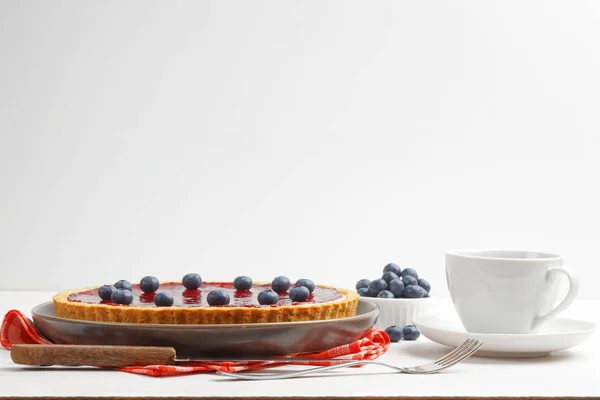 Homemade cheesecake with berry jelly and cup of tea or coffee on white wooden table. Front view. Copy space.