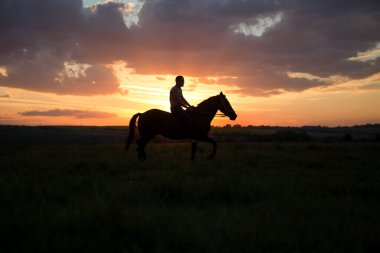 Gün batımında at süren bir adam.