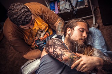 Professional tattooer makes tattoo in tattoo parlor clipart