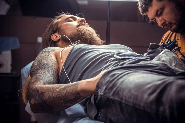 Professional tattooist working tattooing in studio./Professional tattooer works in salon.