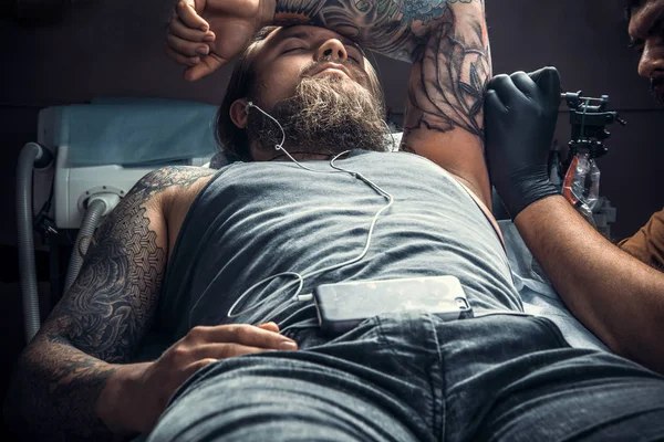 Master making a tattoo in tattoo parlor./Professional tattooist at work in tattoo studio.