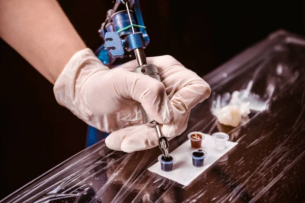 Tatuagem artista está ganhando a tintura em uma máquina de tatuagem — Fotografia de Stock