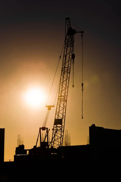 Industriellt byggande kran och byggnaden silhuetter över solen på sunset — Stockfoto