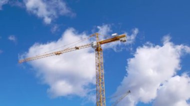 Mavi gökyüzünde Cumulus bulutları olan bir vinç. Zaman ayarlı. İnşaat alanı.