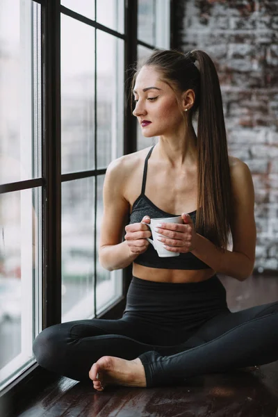 Young Woman in Her Pajamas Sitting in a Window Drinking out of a Mug