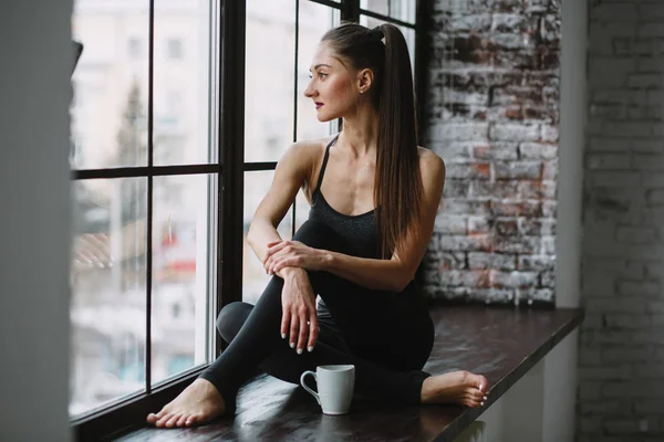 Young Woman in Her Pajamas Sitting in a Window Drinking out of a Mug