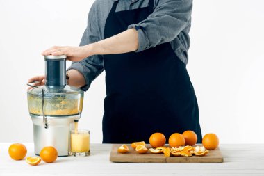 Bir önlük giyiyor, sağlıklı portakal suyu hazırlama, modern elektrikli meyve sıkacağı, sağlıklı yaşam konsepti üzerine beyaz arka plan kullanarak anonim adam