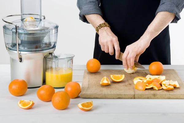 Anonieme man dragen van een schort, voorbereiding van gezonde sinaasappelsap, met behulp van moderne elektrische juicer, gezonde levensstijl concept op witte achtergrond — Stockfoto