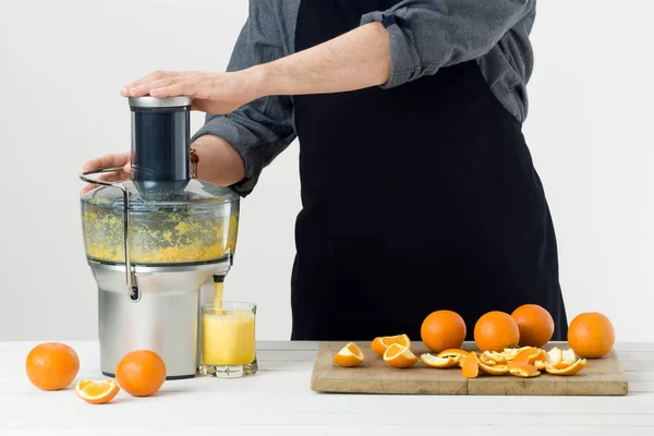 Анонімний чоловік у фартуху, готує здоровий апельсиновий сік, використовуючи сучасну електричну соковижималку, концепцію здорового способу життя на білому тлі — стокове фото