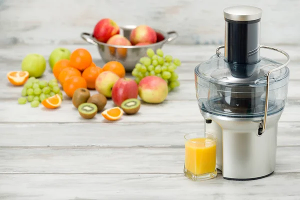 Presse-fruits électrique moderne, divers fruits et verre de jus fraîchement fait, concept de mode de vie sain — Photo