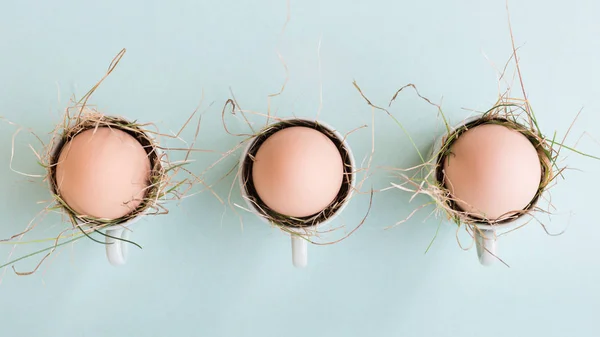 Uncolored natural easter eggs in espresso cups; happy easter concept; green minimalist easter background — Stock Photo, Image
