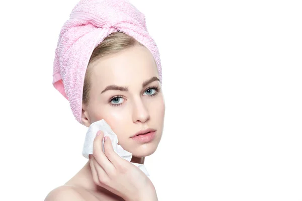 Attractive young blond woman with her hair wrapped in a towel, removing make up. Pretty girl with perfect complexion cleansing her face using soft face wipe . Isolated on white background with copy space. — Stock Photo, Image