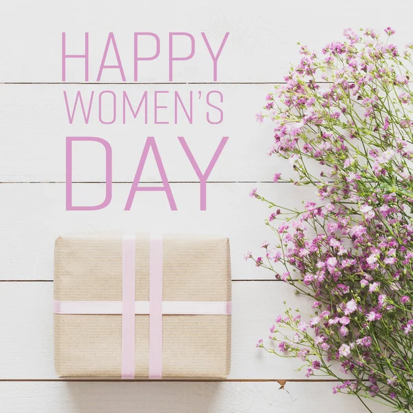 Table en bois blanc avec des fleurs roses et un cadeau, concept de journée des femmes — Photo