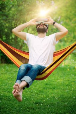 Genç adamın sanal gerçeklik gözlükleri Bahçe bir hamakta rahatlatıcı giydiğini sakallı. Yaşam tarzı Vr eğlenceli ve kavram rahatla