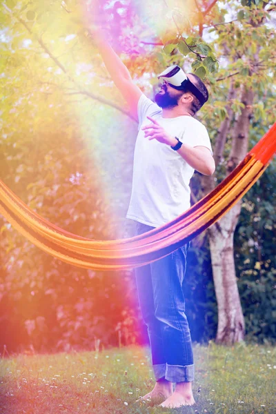 Ein junger bärtiger Mann mit Virtual-Reality-Brille amüsiert sich in seinem Garten. Lifestyle vr Spaß- und Entspannungskonzept — Stockfoto