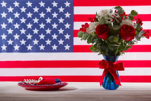 Mesa con hermoso ramo azul rojo y blanco y ajuste de mesa frente a la bandera americana — Foto de Stock