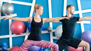 Güzel bir çift bir stüdyoda Yoga yapıyor. Gençler savaşçı yoga sınıfındaki poz. Yoga grup kavramı