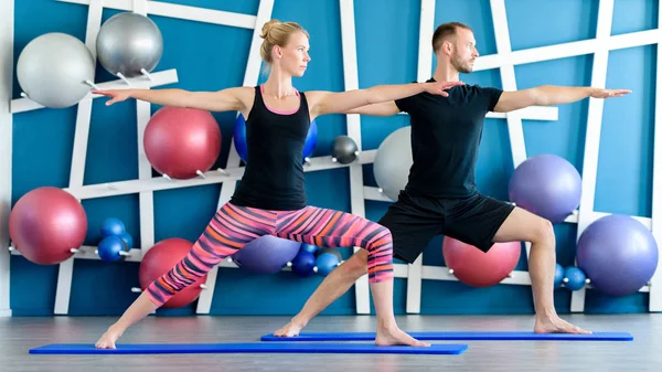 Güzel bir çift bir stüdyoda Yoga yapıyor. Gençler savaşçı yoga sınıfındaki poz. Yoga kavramı.