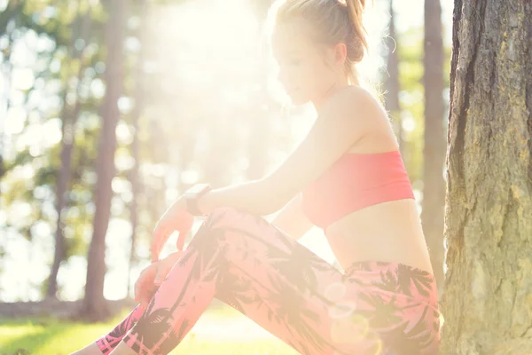 Aantrekkelijke sportieve vrouw dragen van slimme horloge het nemen van een pauze na training sessie. Levensstijl afbeelding met sterke lensflare — Stockfoto