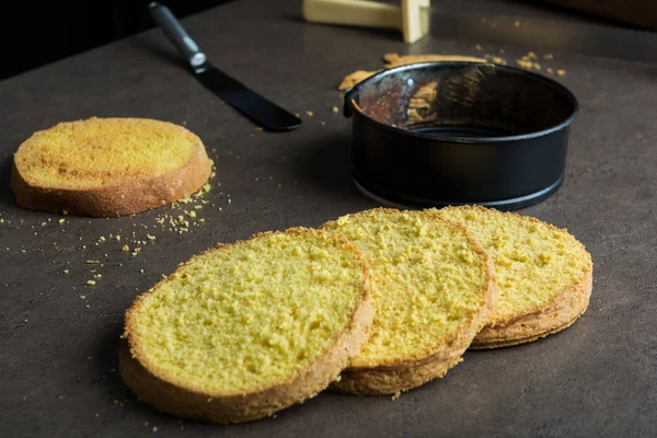 Freshly baked sponge cake cut into four layers, with cake baking form and spatula on kitchen counter — Stock Photo, Image