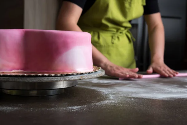Oigenkännliga kvinna förbereder rosa fondant kaka utsmyckning, fokus på kakan — Stockfoto