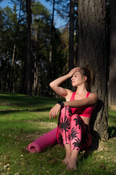 Jovem mulher atlética atraente vestindo relógio inteligente está desfrutando de últimos raios de sol para o dia após seu treino em uma floresta . — Fotografia de Stock