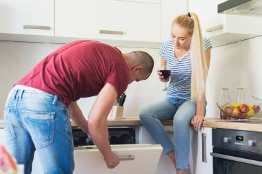 Çekici genç beyaz adam bulaşık makinesi, mutfak tezgahına oturmuş kız arkadaşı süre açılış kırmızı şarap tutar