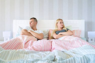 Upset young couple having marital problems or a disagreement sitting side by side in bed facing in opposite directions ignoring one another clipart