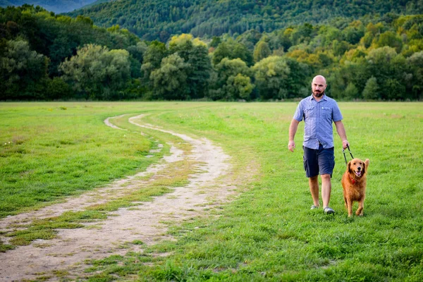 Young handsome Hipster man taking his family pet dog golden retriever for a walk in a park — Stock Photo, Image