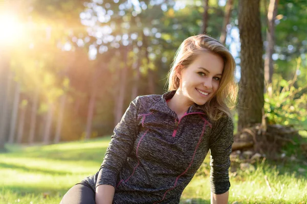 Aantrekkelijke lachende jonge blonde vrouw, het dragen van sportkleding, ontspannen na training in een forest — Stockfoto