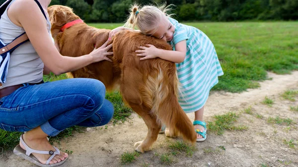 Gadis pirang kecil yang manis tersenyum dan memeluk anjing peliharaannya golden retriever — Stok Foto