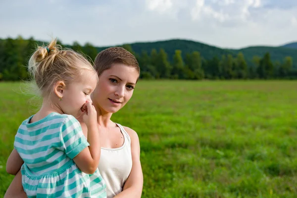 Attractive young mother carrying preschool daughter in her arms during a walk through a meadow — Stock Photo, Image