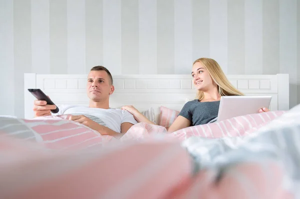 Unga älskande par i sängen, titta på TV och surfar webben med digital tablett — Stockfoto