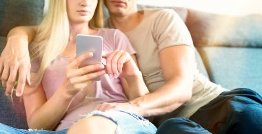 Genç unrecognisable çift kanepede smartphone modern evlerine kontrol sarılma. Örümcek ağı browsing hareket eden telefon, tutan kadın.