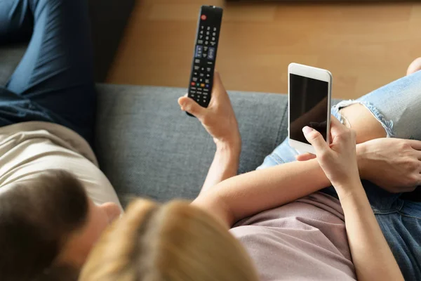 Unga oigenkännliga par hemma, tittar på TV och textning — Stockfoto