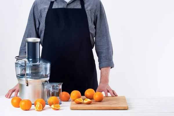 Uomo anonimo che indossa un grembiule, prepara succo d'arancia appena fatto, utilizzando spremiagrumi elettrici moderni, concetto di disintossicazione stile di vita sano su sfondo bianco — Foto Stock