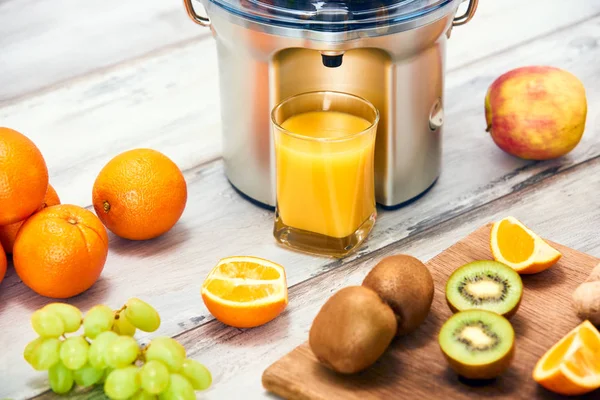 Modern electric juicer, various fruit and glass of freshly made juice, healthy lifestyle detox concept, close up — Stock Photo, Image