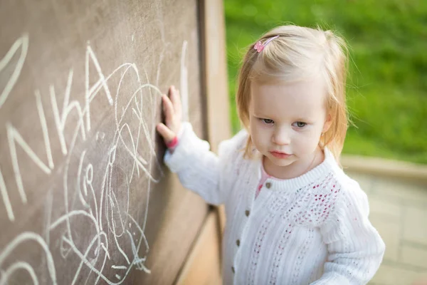 Linda niña dibujando en pizarra. Niña pequeña divirtiéndose al aire libre, sosteniendo tiza y dibujo . —  Fotos de Stock