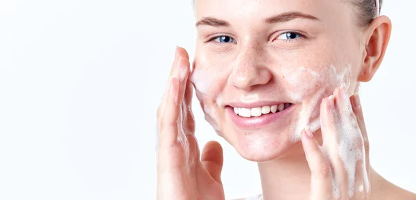 Remaja skincare. Senyum gadis remaja cantik dengan bintik-bintik dan mata biru menggunakan pembersih berbusa. Konsep cuci wajah terisolasi pada latar belakang putih . — Stok Foto